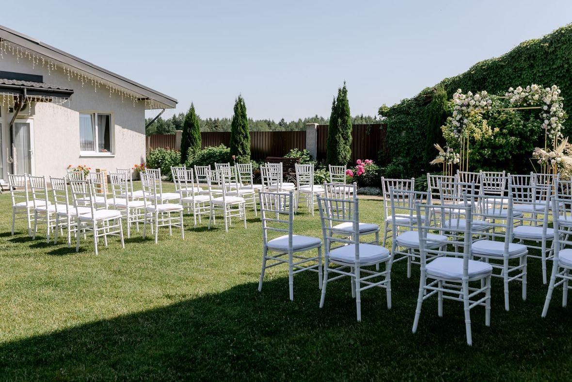 Krzesła ustawione w ogrodzie przed prostym łukiem do ceremonii ślubnej
